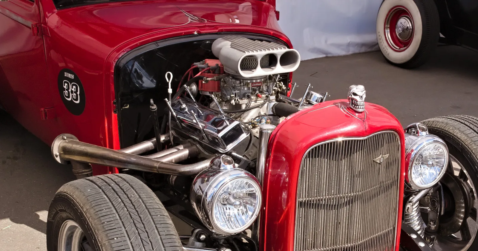 A red hot rod with its engine out in the open, a chrome blower scoop on top
